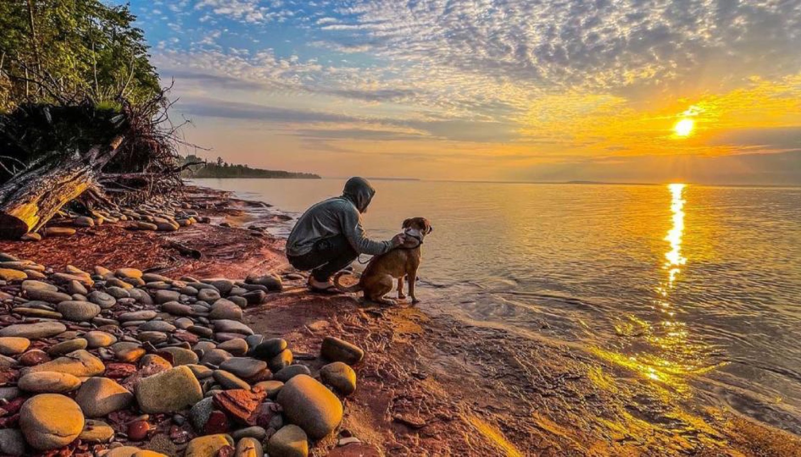 A hiker and dog on a rocky Lake Superior shore at sunset